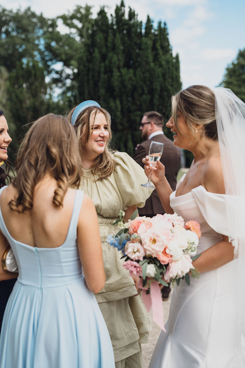 A colour image of a bride chatting with her guests wearing beautiful summer pastel colour dresses at Combermere Abbey Shropshire - wedding planning by Soiree Studio.
