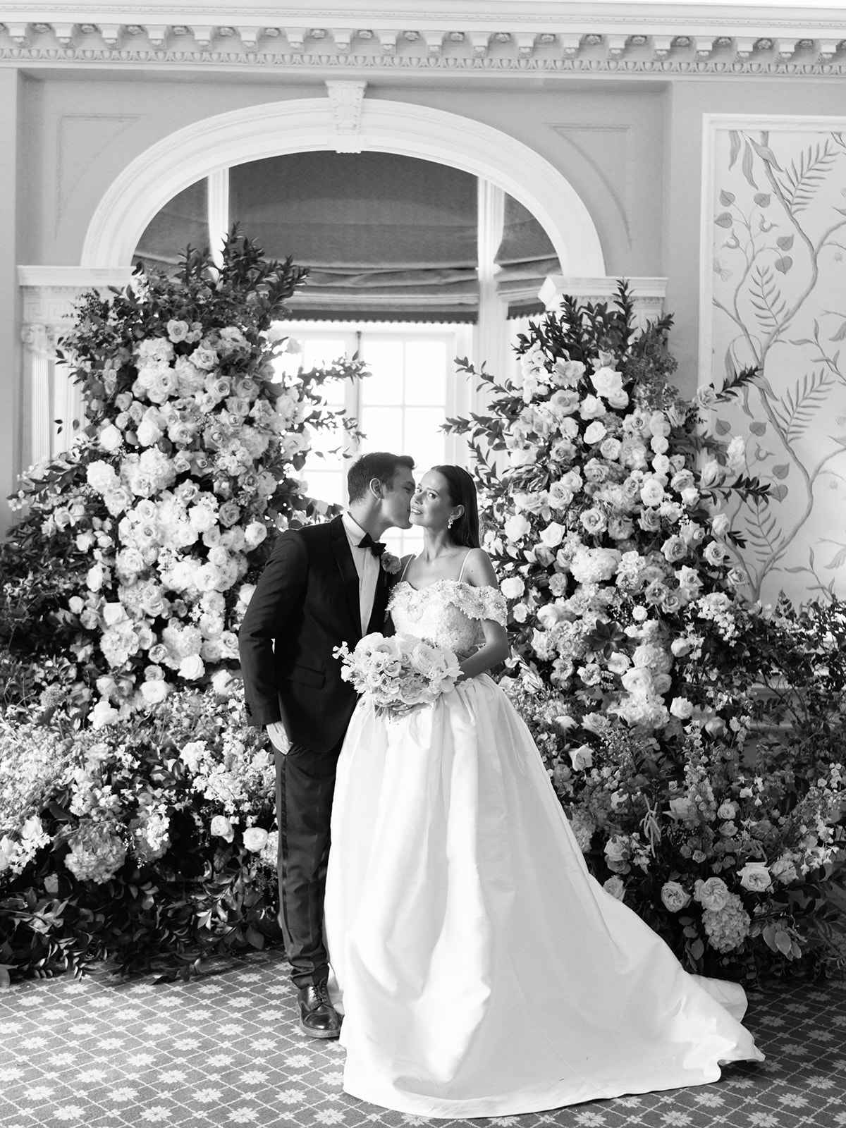 A black and white image of a wedding ceremony with huge floral backdrop at Pal&eacute; Hall in Wales. Planned by Soir&eacute;e Studio.