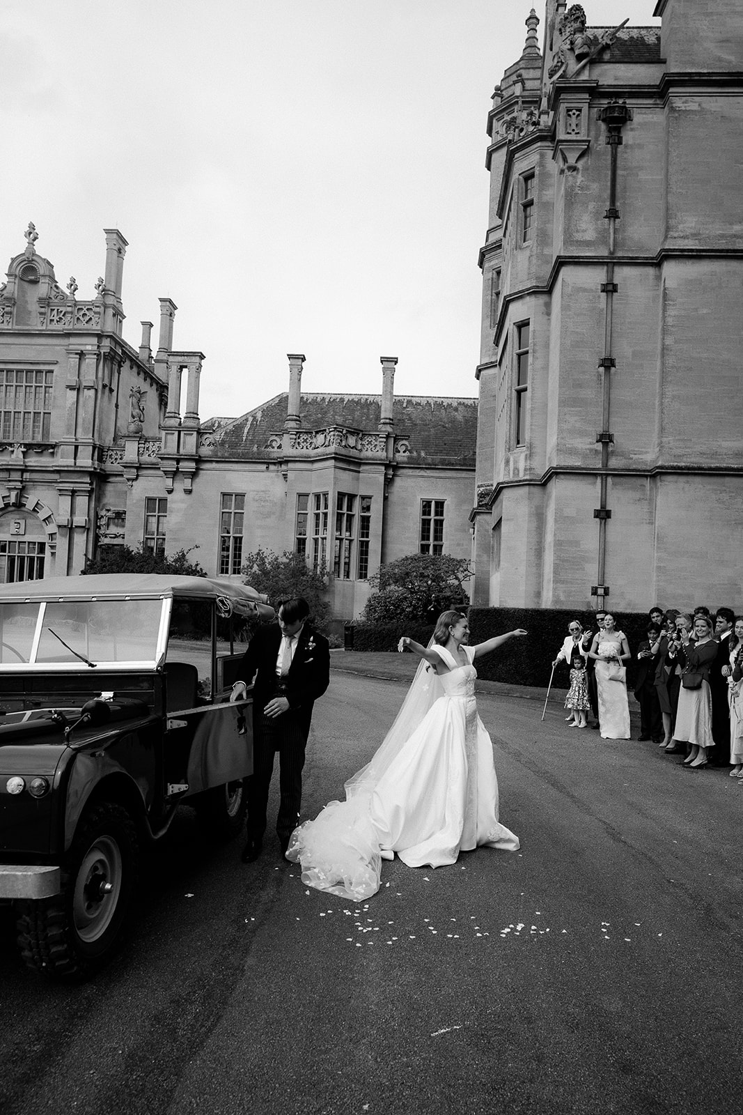 A black and white image of a bride and groom arriving at their wedding at exclusive use wedding venue Harlaxton Manor with wedding planned by Soir&eacute;e Studio